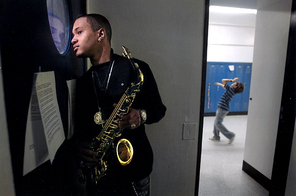 josh waits his turn to perform with his sax while others practice in the hall behind him.